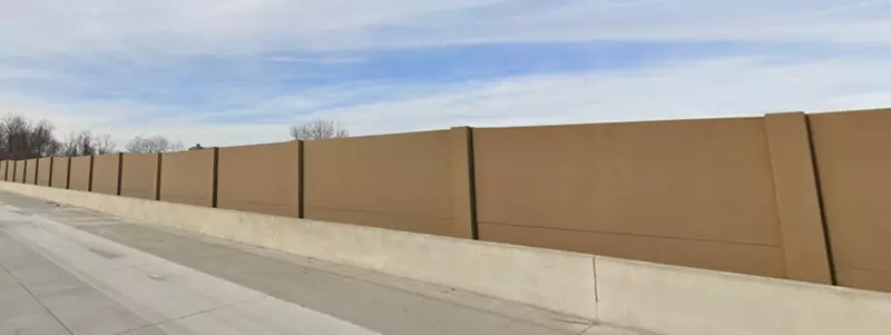 An image of a brown-colored concrete sound wall along a roadway.